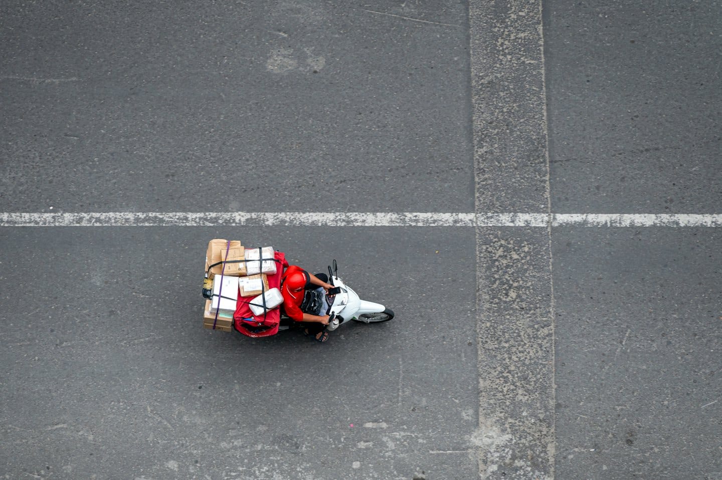 Autista di consegne su uno scooter con scatole di cartone impilate.