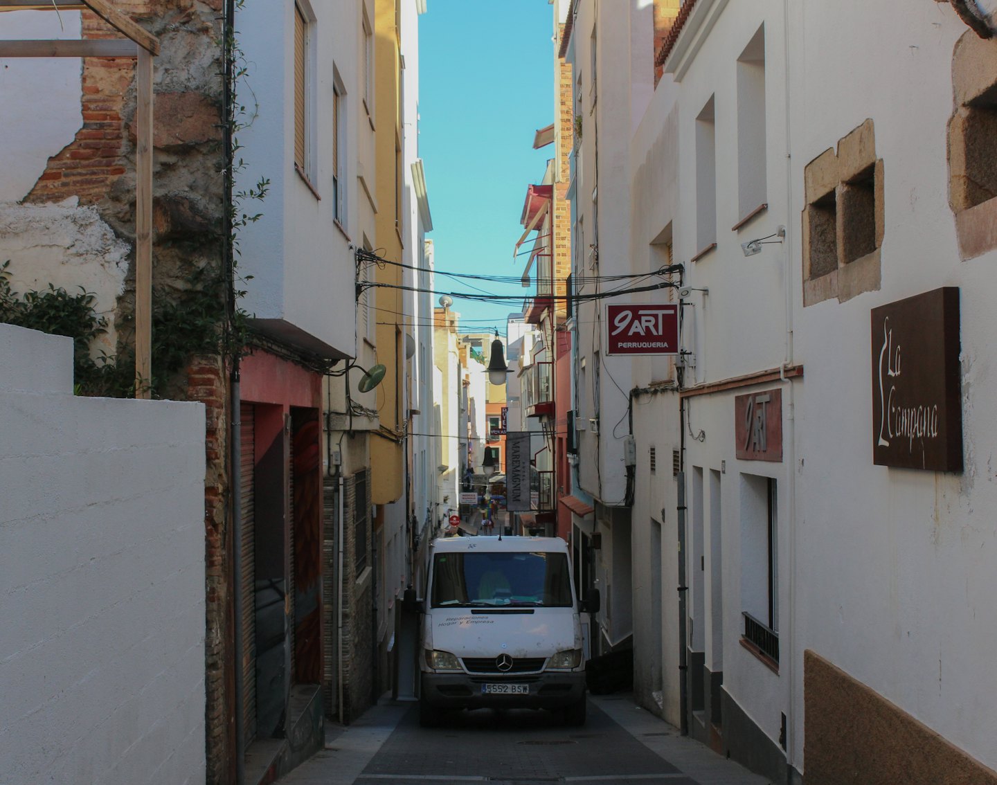 Un furgone bianco parcheggiato in una stretta strada urbana.