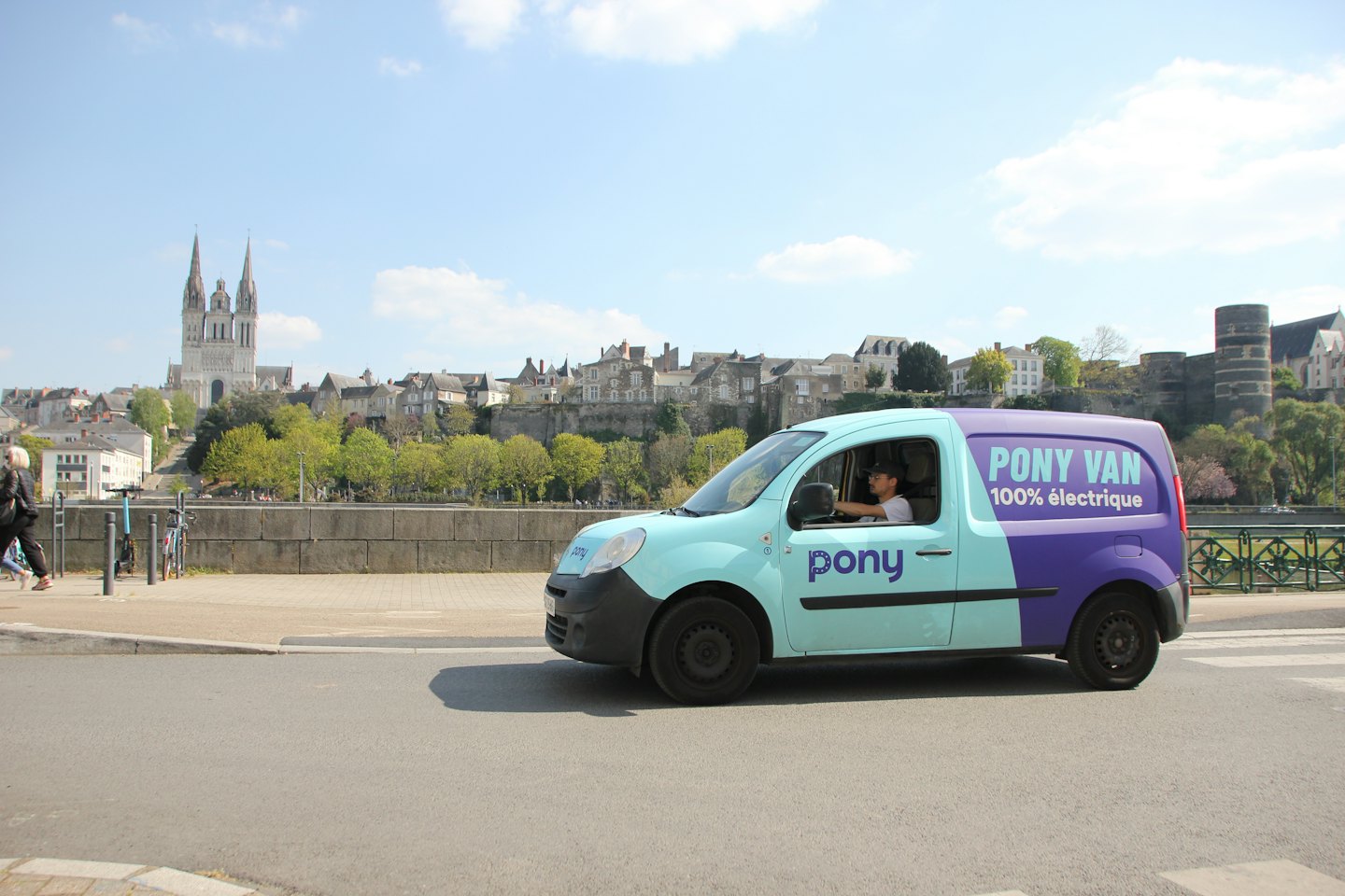 Un uomo guida un furgone blu e viola per le consegne in città.
