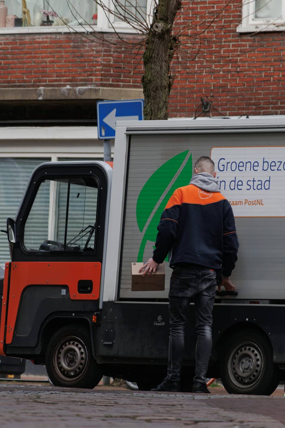 Addetto alle consegne tiene un pacco accanto a un veicolo elettrico in strada.